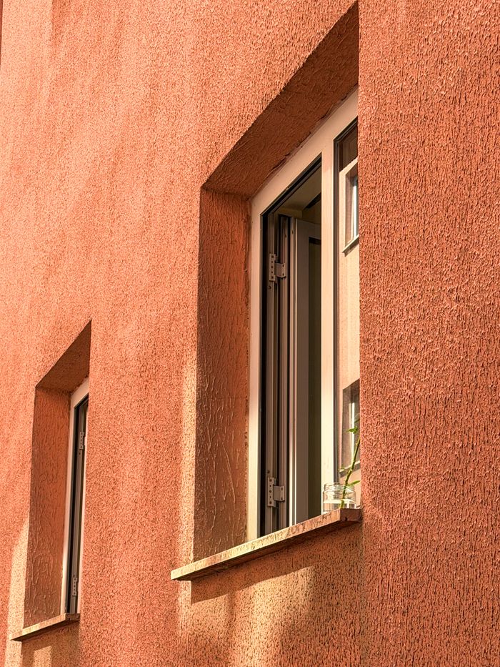 Strona główna A sunlit terracotta wall featuring an open window, perfect for architectural visuals.