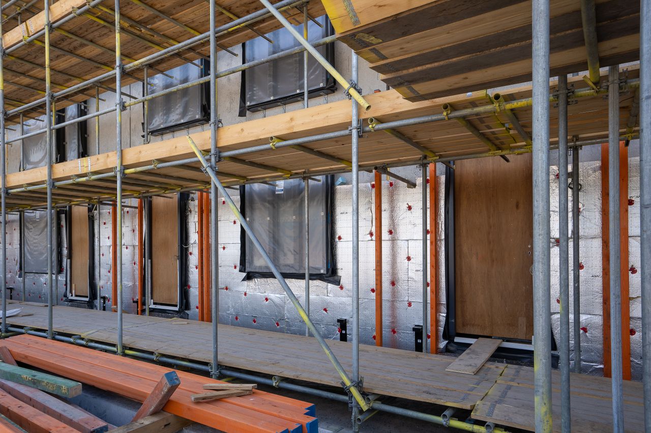 Mastering the First Impression: Your intriguing post title goes here Scaffolding at a residential building under construction with windows and insulation sheets visible.